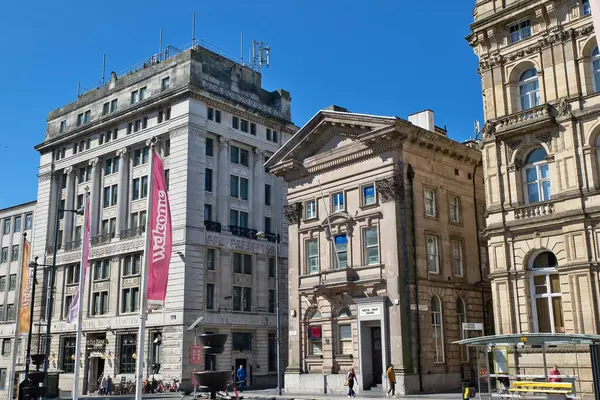 Liverpool, İngiltere 'de açık mavi bir gökyüzü altında, insanlar ve sokak mobilyaları ile Ulusal Banka da dahil olmak üzere çeşitli binaların dış görüntüsü..