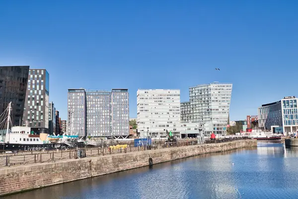 Şehir deniz manzaralı modern binalar ve açık mavi gökyüzü altında yanaşmış gemiler. Liverpool, İngiltere 'de ön planda bir tuğla iskele duvarı var..