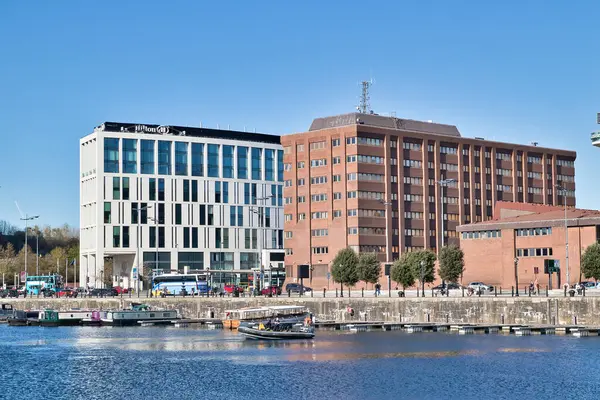 Tekneler ve İngiltere 'nin Liverpool kentinde açık mavi gökyüzü ile bir su yoluna sınır çizen binalar (Hilton da dahil) kentsel manzara.