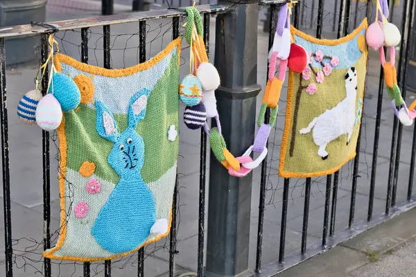 Örülmüş Paskalya süslemeleri siyah metal bir çitten sarkıyor. İki panelde, Ripon, Yorkshire, İngiltere 'de örülmüş yumurta ve zincir içeren bir tavşan ve bir lama var..