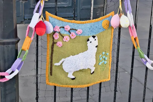 Çitin üzerine örülmüş bir süsleme. Koyun, çiçek ve Paskalya yumurtalarının bulunduğu bir manzara. Ripon, Yorkshire, İngiltere 'de renkli bir örgü zinciri ile asılmış..