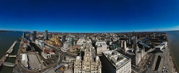 Liverpool, İngiltere 'nin panoramik hava manzarası, açık mavi gökyüzü altında Liver Binası, şehir manzarası ve Mersey Nehri yer almaktadır..