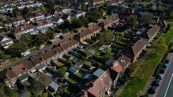 Morden, Londra, İngiltere 'de caddelerde bahçeli, ağaçlı ve park halindeki arabaların bulunduğu banliyö manzaralı evler..