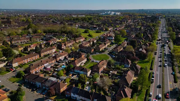 Morden, Londra, İngiltere 'de açık mavi gökyüzünün altında evleri, ağaçları ve trafiği olan çok şeritli bir banliyö manzarası..