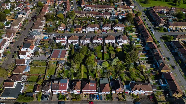 Morden, Londra, İngiltere 'de park halindeki arabalı evler, yeşil çimenler, ağaçlar ve caddelerin bulunduğu bir banliyö manzarası..