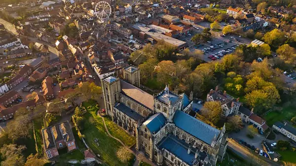 Bir kasaba, ağaçlar, otopark ve dönme dolap ile çevrili bir katedralin havadan görünüşü. Hepsi de Ripon, İngiltere 'de güneşin doğuşu ya da batışının sıcacık ışıklarıyla yıkanmış..