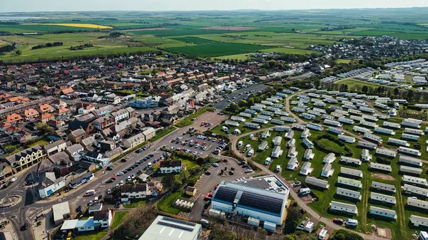 Tarlaları çevreleyen bir kasabanın ve karavan parkının havadan görüntüsü. Özellikler, evler, arabalar, yollar, yeşil alanlar ve İngiltere 'nin Deniz Evleri köyünde bir güneş paneli binası.