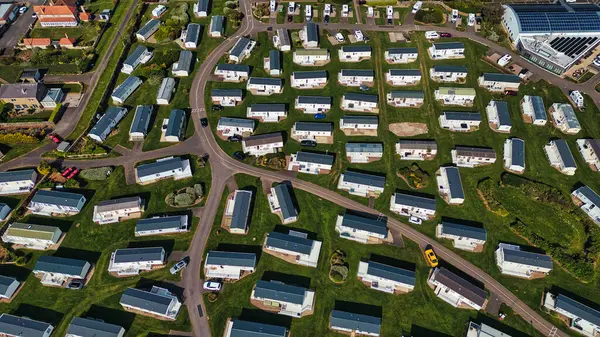 Statik bir karavan parkının havadan görünüşü, İngiltere 'deki Deniz Evleri Köyü' nde parlak bir gökyüzü altında sıralanmış kervanlar, çimenlik alanlar ve yollar..