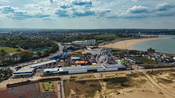 İngiltere 'nin Sandhaven Sahili' nde parçalı bulutlu bir gökyüzünün altında bir sahil, kasaba ve su kütlesinin yanındaki bir kıyı eğlence parkının havadan görünüşü..