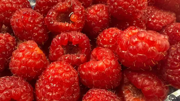 Taze kırmızı ahududu yığınının yakın çekim görüntüsü. Bileşim çerçeveyi meyvenin canlı rengi ve eşsiz dokusu ile doldurur..