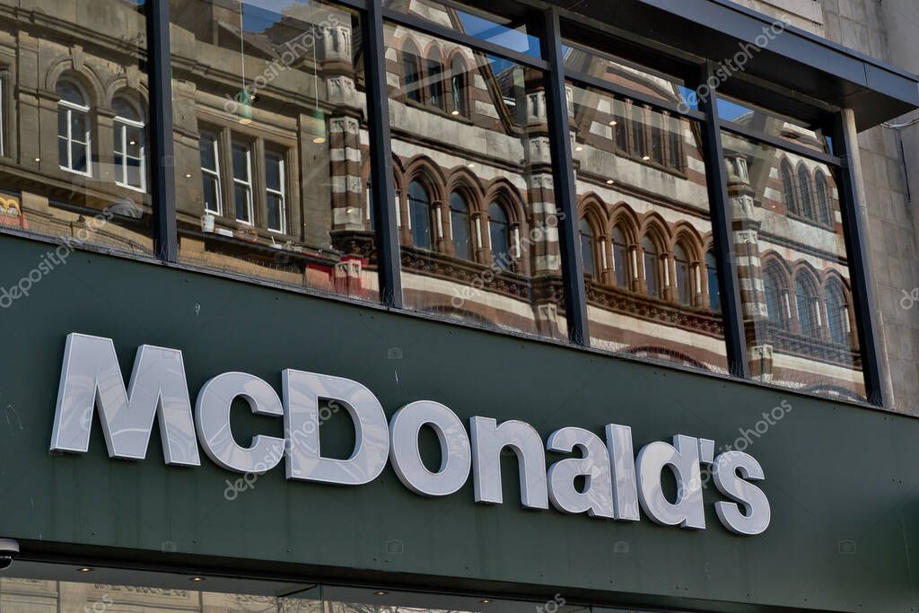 McDonald's sign is in the foreground, with a building reflected in the glass behind it in Liverpool, UK.