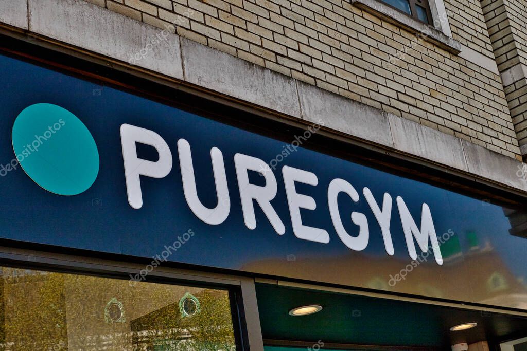 A medium shot of a PureGym sign on a building. The sign is navy blue with white lettering and a teal circle in Wimbledon, London, UK.
