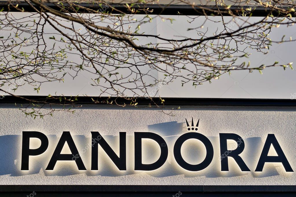 Pandora sign on a white textured wall with branches and budding leaves in the foreground in Harrogate, Yorkshire, UK.