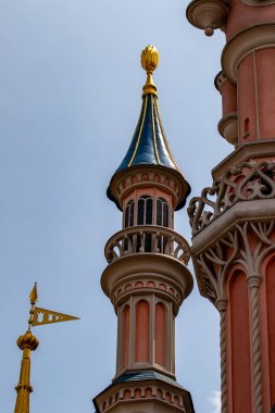 Açık mavi gökyüzüne karşı süslü, pembe ve bej renkli kale kulelerinin yakın çekimi. Altın aksanlar Fransa 'nın Disneyland şehrindeki mimariyi vurguluyor.