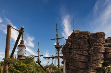 Gemi direkleri, ahşap bir direkte bir fener, kayalık bir oluşum ve Fransa 'nın Disneyland şehrinde ince bulutlu mavi bir gökyüzü..