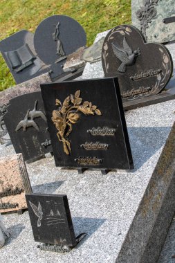 Cemetery scene with black granite headstones featuring engravings and raised designs, arranged on a gray granite surface, with grass in the background in Giverny, France.
