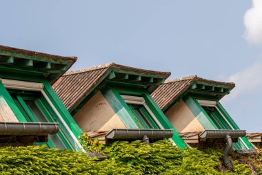 Yeşil çerçeveli üç yurt penceresi, kahverengi çatıları ve duvarı kaplayan sarmaşık, Fransa 'nın Giverny şehrinde birkaç beyaz bulutlu mavi bir gökyüzüne karşı kurulmuş..