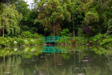 Fransa 'nın Giverny kentinin arka planında parlak yeşil kemerli bir yaya köprüsü ile yansıtıcı bir gölet oluşturan yemyeşil yapraklar çerçevelenir..