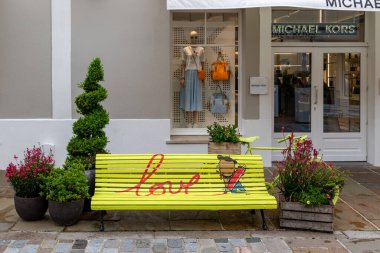 La Vallee Village, Fransa 'da vitrininde bir manken bulunan boyanmış bir bank, bitkiler ve Michael Kors mağazasıyla sokak manzarası..