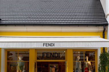 Siyah kiremit çatılı parlak sarı bir FENDI mağazası, güneşlik, vitrin vitrinleri ve Fransa 'nın La Vallee Köyü' nde görünür bir açık kapı..