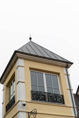 Fransa 'nın başkenti La Vallee' de beyaz gökyüzüne karşı gri çatılı, beyaz çerçeveli, pencereli ve dekoratif siyah demiri olan sarı bir binanın alçak açılı görüntüsü..