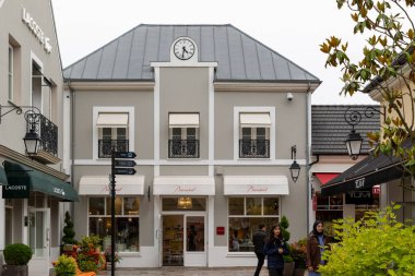 Bakara mağazasının önünde, Lacoste ve Tumi dükkanlarının bitişiğindeki perakende satış alanı ve Fransa 'nın La Vallee Köyü' ndeki mağazanın önünde yürüyen bazı insanlar var..
