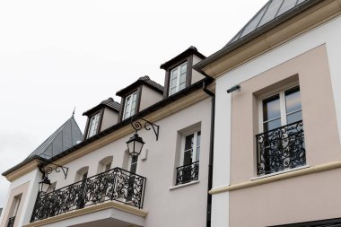 Pencereleri, yurtları ve dekoratif balkonları olan binaların alçak açılı görüntüsü Fransa 'nın La Vallee Köyü' nde gökyüzüne karşı dövülmüş demir balkonlar..