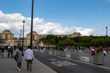 Paris street scene with people, architecture, and a partially cloudy sky. Focus on the street and buildings in the background.