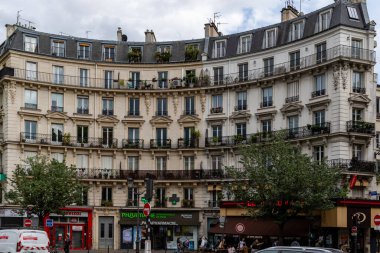 Paris 'teki kıvrımlı, çok katlı bir binada mimari detaylar, bitkilerle dolu balkonlar ve zemin kattaki mağazalar yer alıyor..