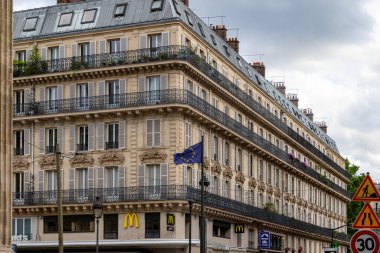 A multi-story building with balconies and shutters, featuring McDonald's restaurants on the ground floor and a European Union flag.