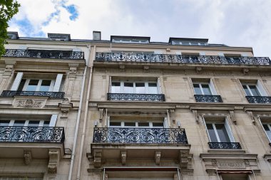 Balkonları ve pencereleri olan bir binanın alçak açılı görüntüsü. Binanın hafif bir taş cephesi var. Süslü, siyah demir parmaklıkları var..