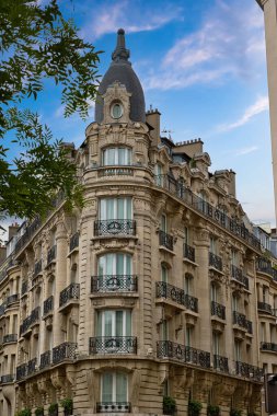 Pencereleri, balkonları, süslü taş işçiliği ve mavi gökyüzüne karşı kendine özgü kubbesi olan detaylı bir köşe binası cephesi..