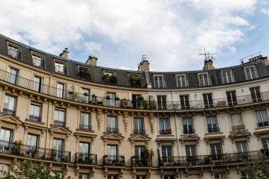 Balkonları, pencereleri ve yukarıda bulutlu bir gökyüzü olan eğimli bir binanın alçak açılı görüntüsü..
