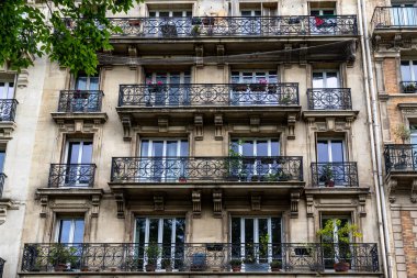 Pencereleri, süslü demir balkonları ve bej ve gri tonlarında mimari ayrıntıları olan çok katlı bir binanın ön cephesi.