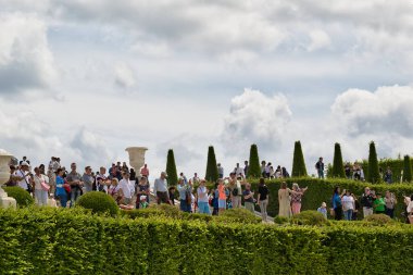 Manikürlü çalılar, konik ağaçlar ve Paris 'teki Versailles Gardens' ta bulutlu gökyüzü olan bir parkta turistler..