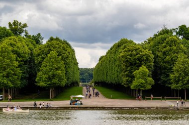 Kanal manzaralı, kayıklı, ağaçlarla kaplı, bulutlu gökyüzünün altında Paris 'teki Versailles Gardens' a giden yol..