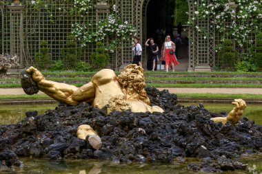 Paris 'teki Versailles Gardens' ın arka planında yürüyen insanların göldeki siyah kayalardan yükselen bir adamın altın heykeli..