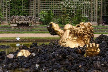 Paris 'teki Versailles Gardens' ta sarmalanmış bahçe zeminine karşı koyan koyu kayalık su özellikli altın heykel..