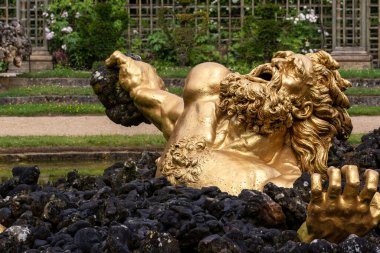 Paris, Versailles Gardens 'daki açık bir bahçede, siyah kayaların üzerinde, bir taşı kavrayan kederli figürün altın heykeli..