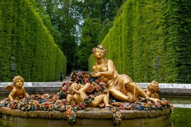 Versailles Gardens, Paris 'teki yeşil çitli bir bahçede çiçek kaplı bir çeşmede altın heykeller..