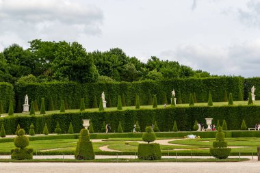 Yeşil çitlerin, heykellerin, heykellerin ve Paris 'teki Versailles Gardens' ta bulutlu bir gökyüzünün altında yürüyüş yollarının olduğu resmi bir bahçe..