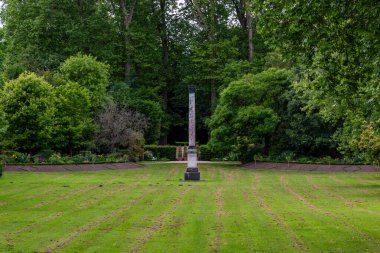 Yeşil ağaçlarla çevrili merkezi mermer bir kolona sahip yemyeşil bir park manzarası ve Versailles Gardens, Paris 'te görünür biçme şekilleri olan manikürlü bir çimenlik..