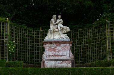 Açık havada, Paris Versailles Gardens 'da ahşap bir çardağın zeminine ve sık yapraklara dayanan mermer bir kaide üzerindeki iki figürü tasvir eden heykel..