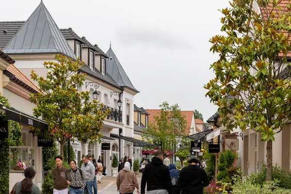 Fransa 'nın La Vallee Köyü' nde bulutlu bir gökyüzünün altında vitrinler, binalar ve ağaçlarla dolu bir kaldırımda yürüyen insanların sokak manzarası..