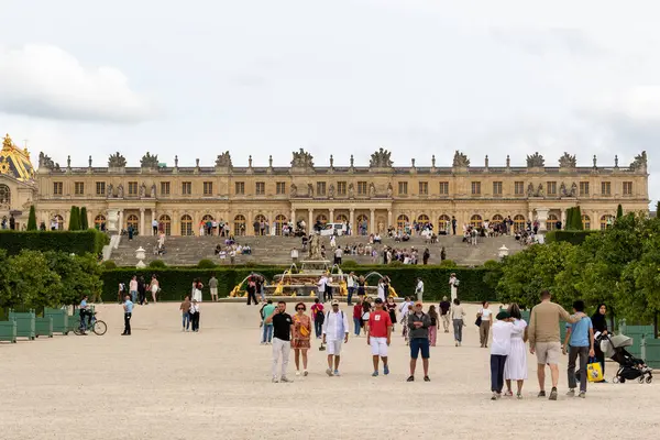 Versailles Sarayı, bulutlu bir günde büyük bir kalabalık, bahçeler ve bir çeşme barındırır..