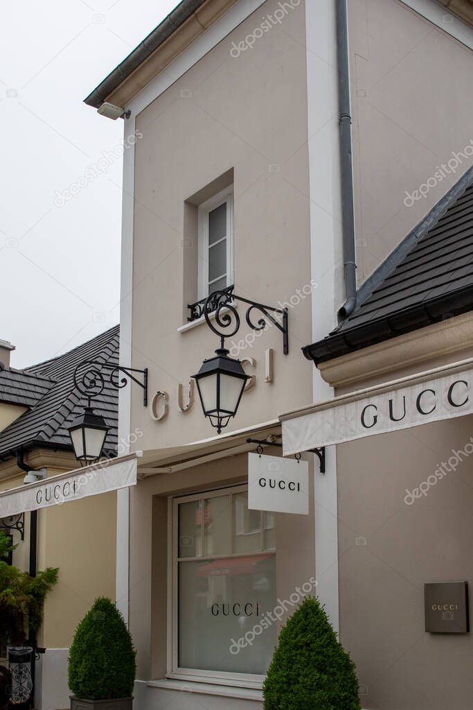 A close-up of a Gucci store facade, showcasing the building's architectural details, signage, and landscaping elements at La Vallee Village, France.