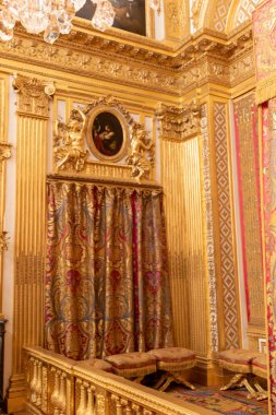 Opulent room corner featuring gold columns, ornate decor, a draped patterned curtain, and cushioned stools, creating a luxurious atmosphere at Versailles Palace, Paris.