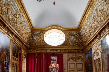 Paris, Versailles Sarayı 'nda beyaz bir tavanın altında altın süslemeler, sanat eserleri, bir avize ve büyük yuvarlak bir pencere bulunan süslü bir oda..