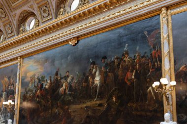 Paris 'teki Versailles Sarayı' nda dekoratif kalıplar ve mimari unsurlar bulunan büyük bir odada süslü altın çerçeveli büyük bir tarihi resmin iç görünümü..
