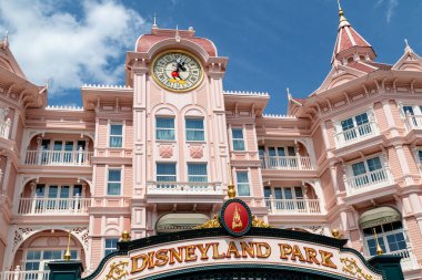 Miki Fare 'nin ellerinin saat yüzünde, Disneyland Paris' te mavi bir gökyüzünün altında yer aldığı büyük bir saat kulesi olan pembe Victoria tarzı bir bina..
